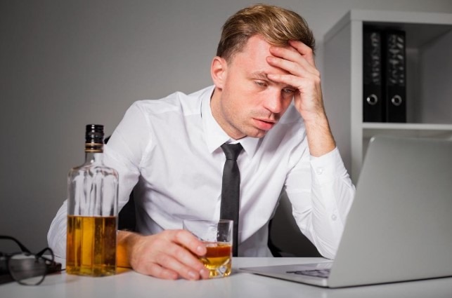 signs someone is an alcoholic - guy sitting at a desk with alcohol