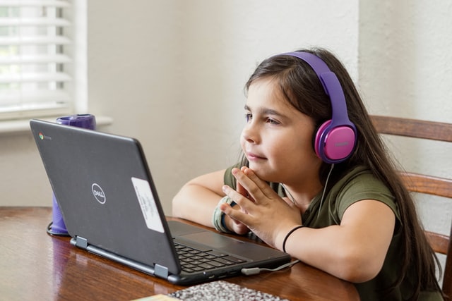 child working on laptop while listing music