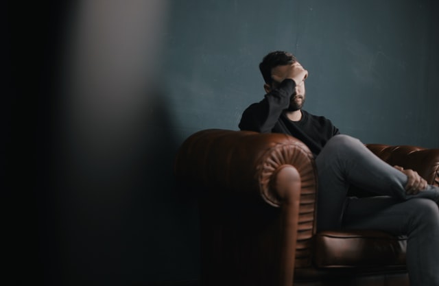 A man sitting on the sofa holding his head due to stress.