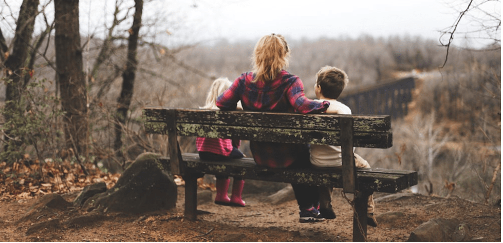 A parent sitting with her kids on a bench.