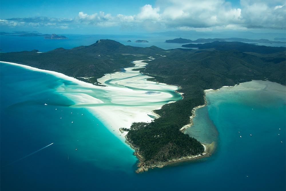 Aerial view of Whitehaven Beach and Hill Inlet in the Whitsundays, featuring brilliant white silica sand swirling through turquoise waters surrounded by lush green islands.